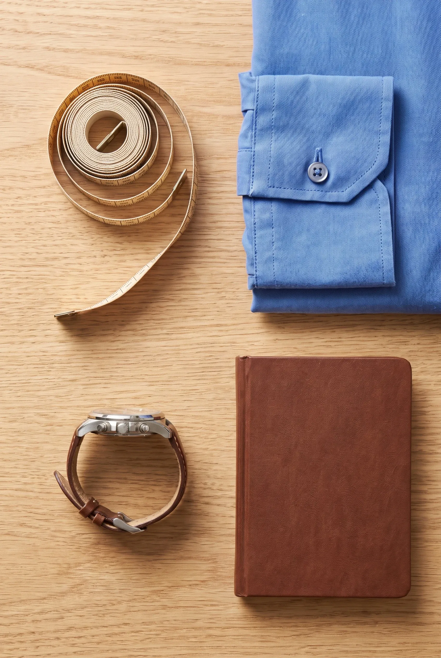 Men's watch beside measuring tape and shirt cuff on an oak desk for quiet sizing reference.