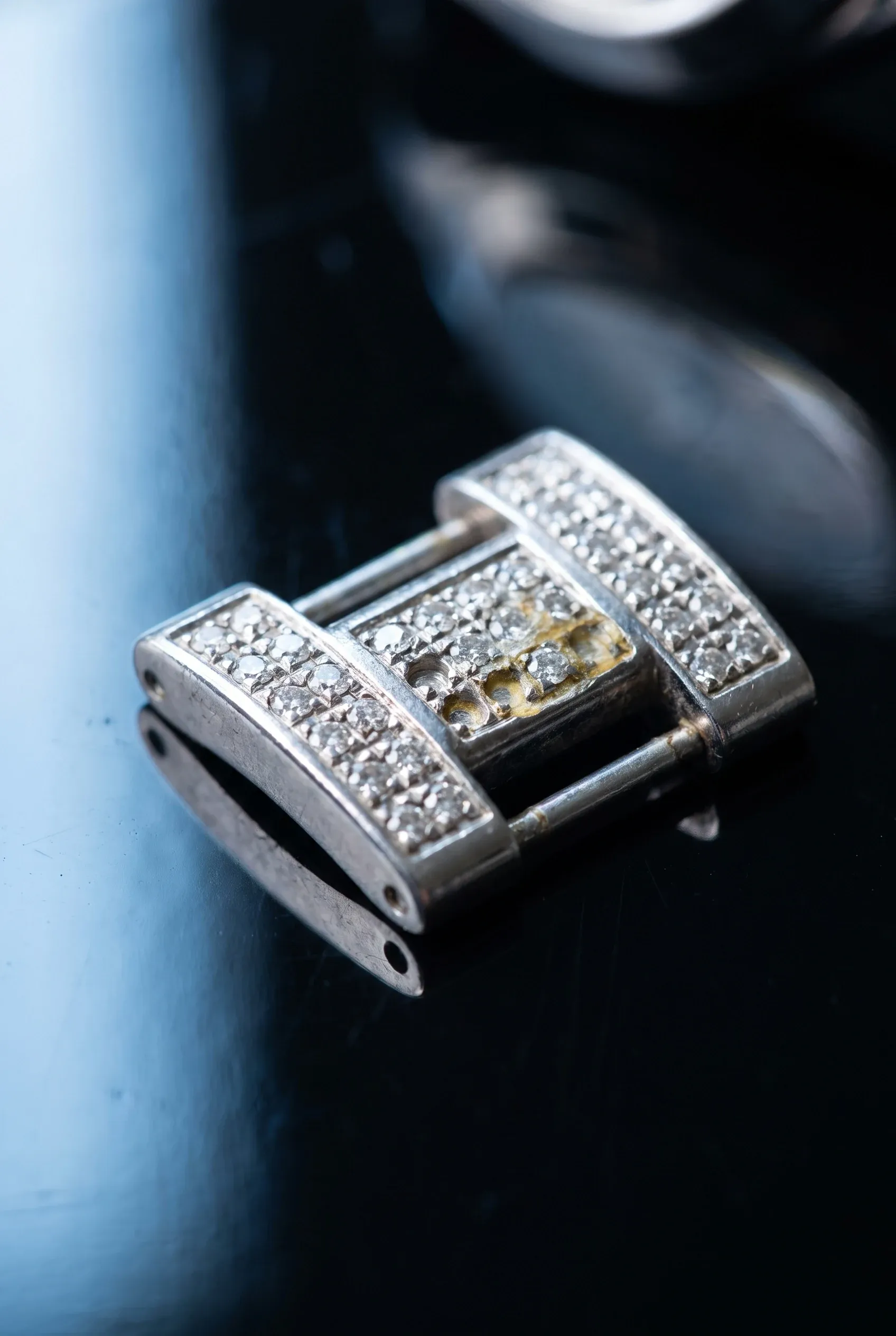 Close-up of an iced bracelet link with empty stone seats and slight adhesive residue near the edge.