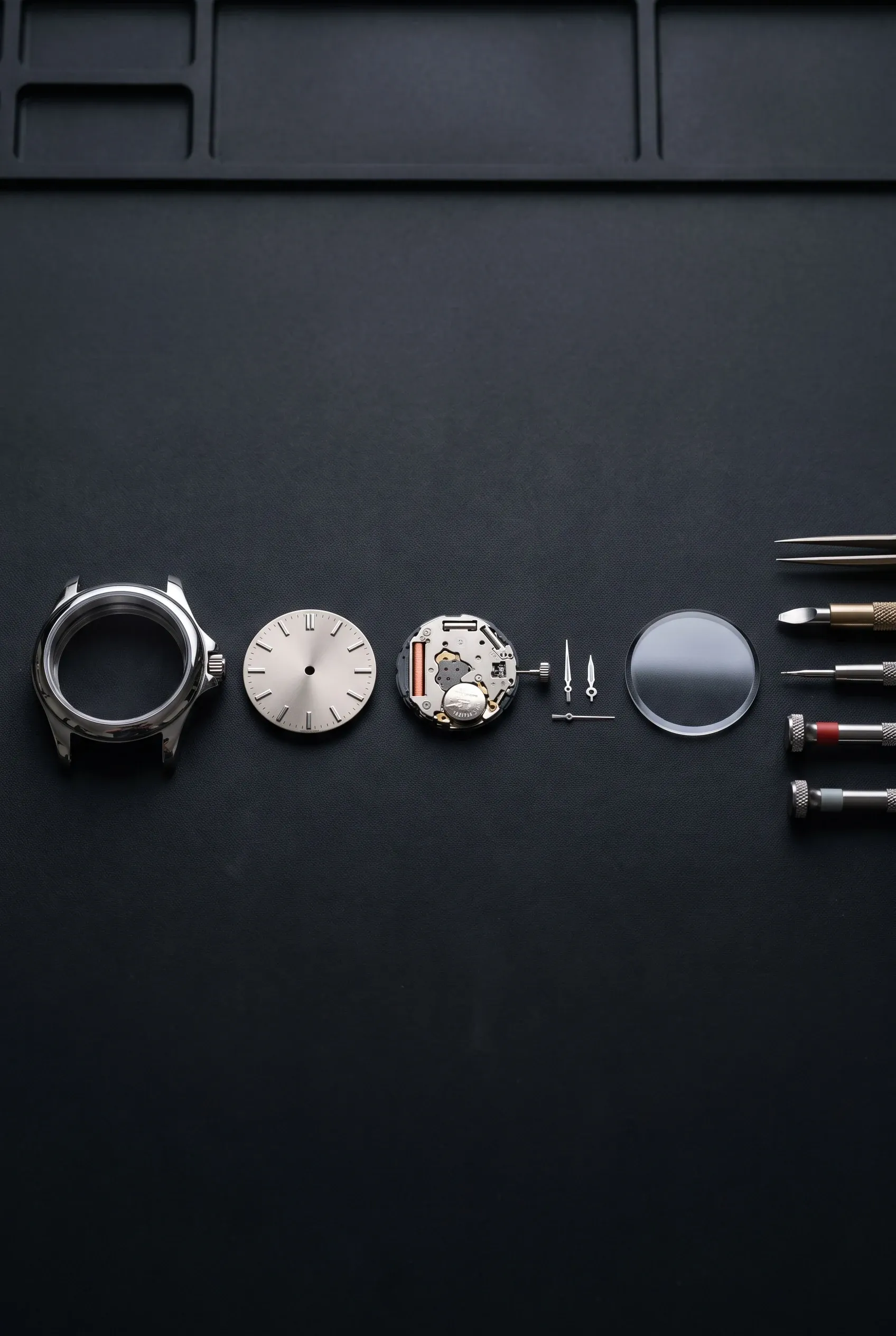 Watch parts laid out for assembly after setting, including dial, movement, crystal and tools.