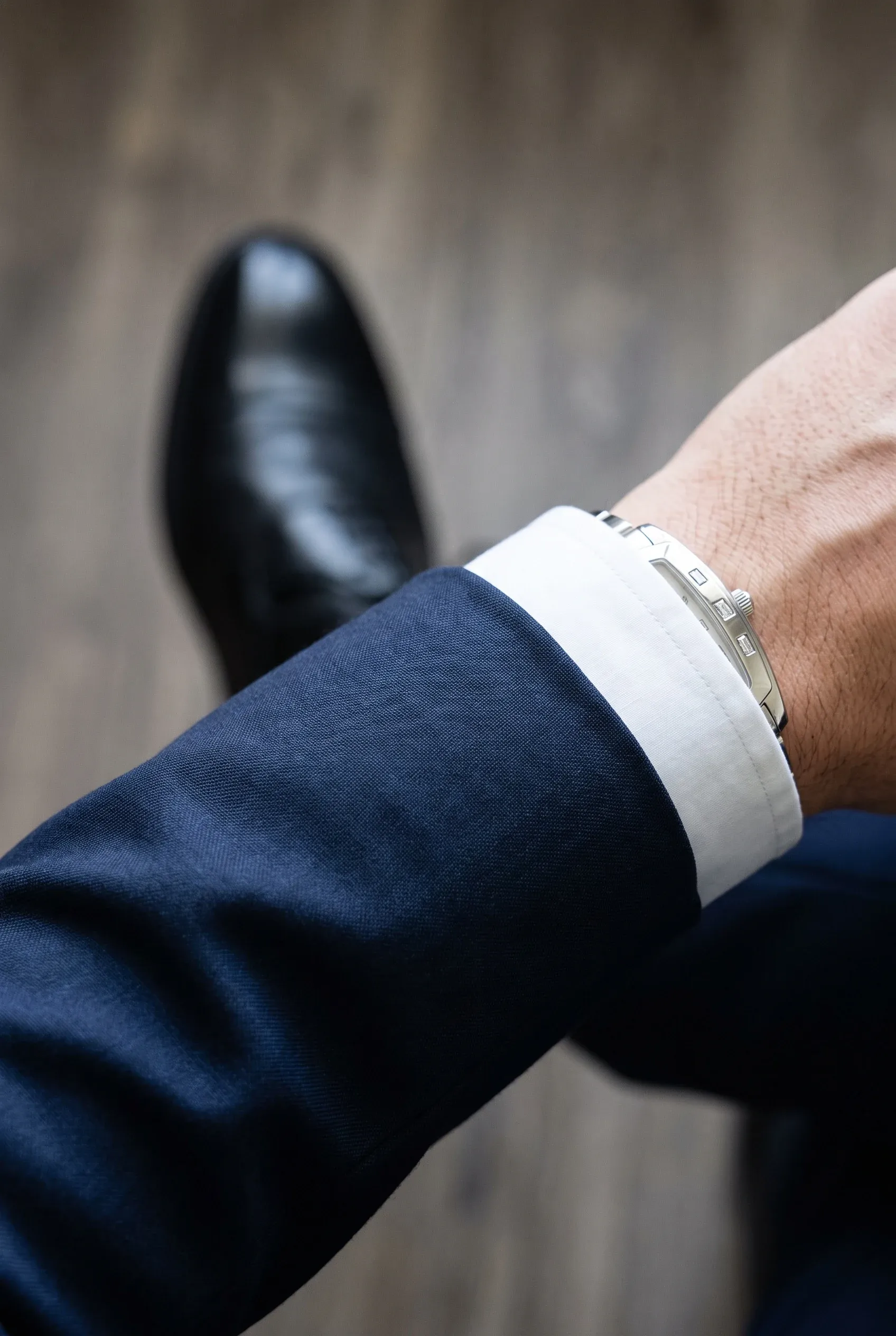 Navy suit sleeve and white shirt cuff framing a silver stone-set watch in soft daylight.