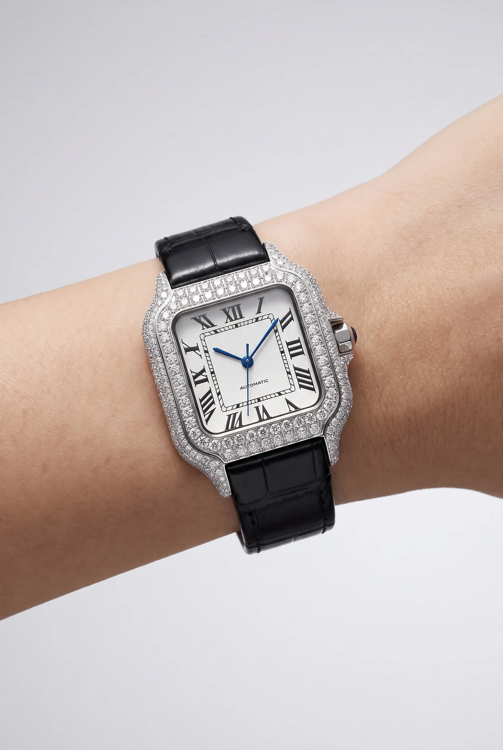 Small wrist wearing a square stone-set women’s watch on a dark leather strap.