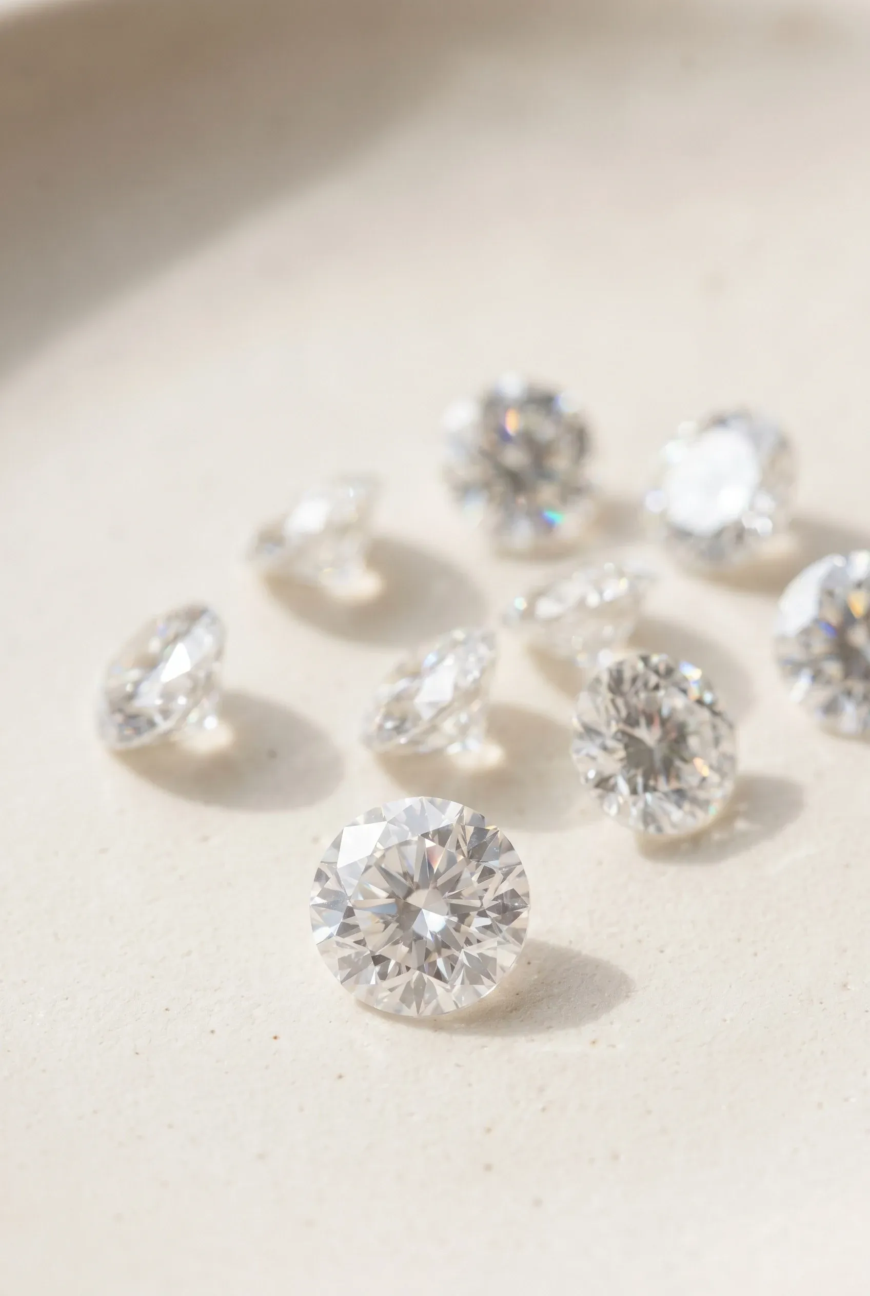 Loose moissanite stones on a pale surface showing bright white sparkle and subtle rainbow fire in daylight.