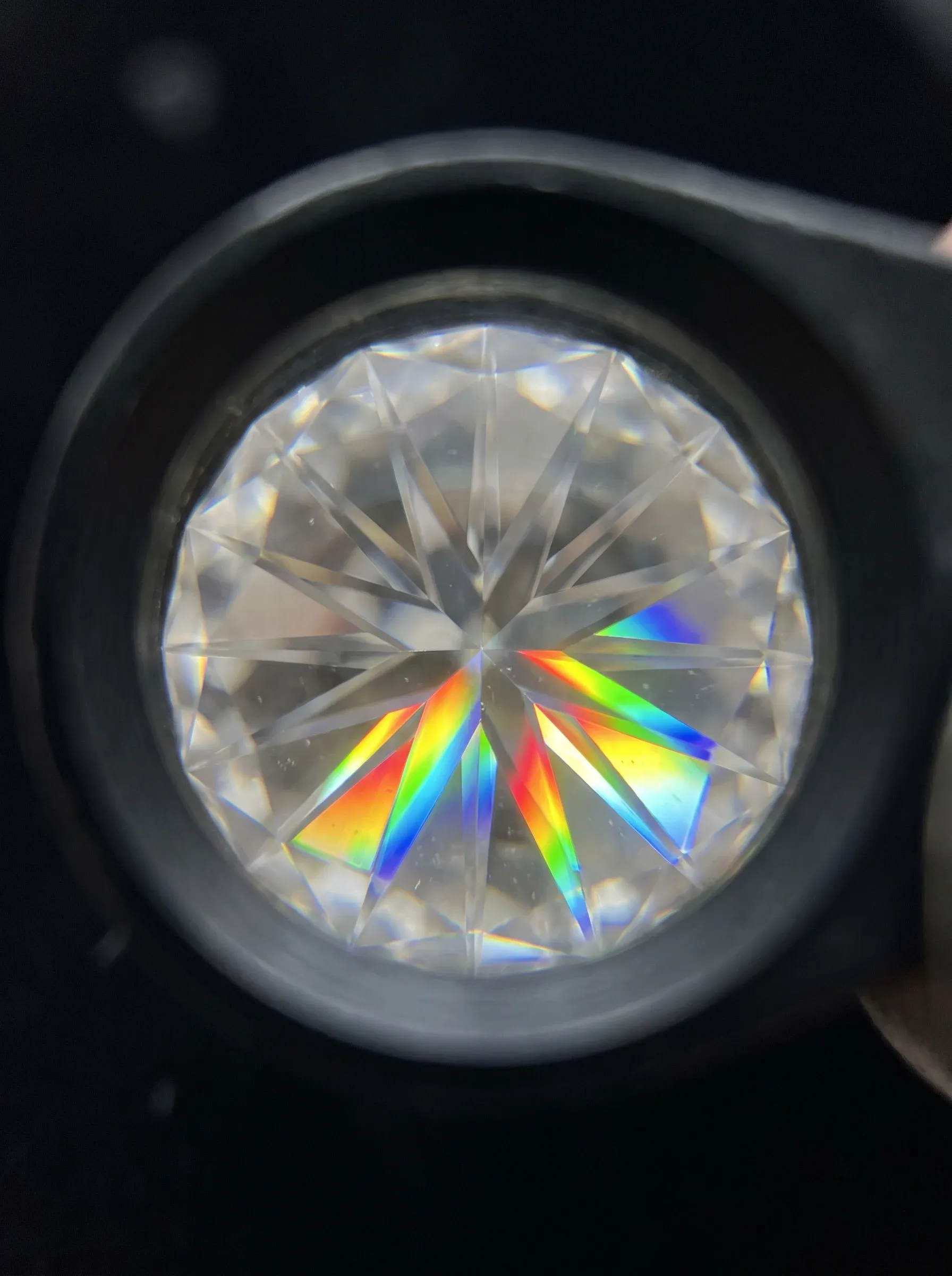 View through a jeweler's loupe of a round brilliant stone splitting light into strong rainbow segments