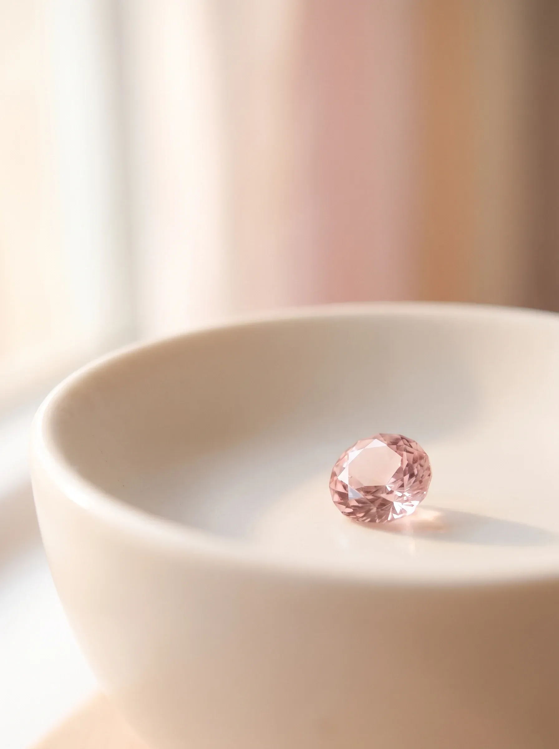 Single blush-pink round stone resting inside a cream ceramic bowl by a bright window