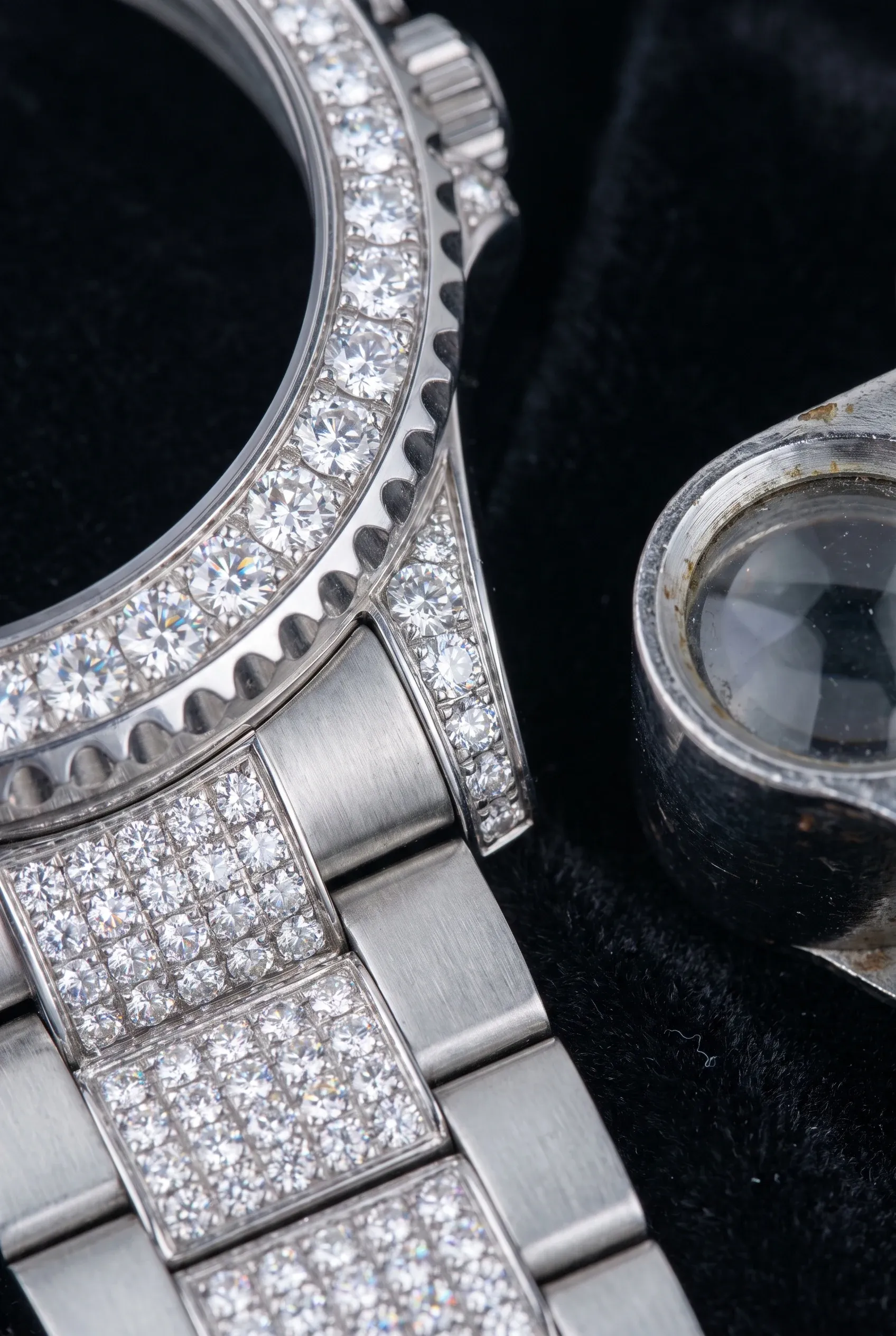 Macro view of a moissanite-set bezel and bracelet beside a loupe on black velvet.