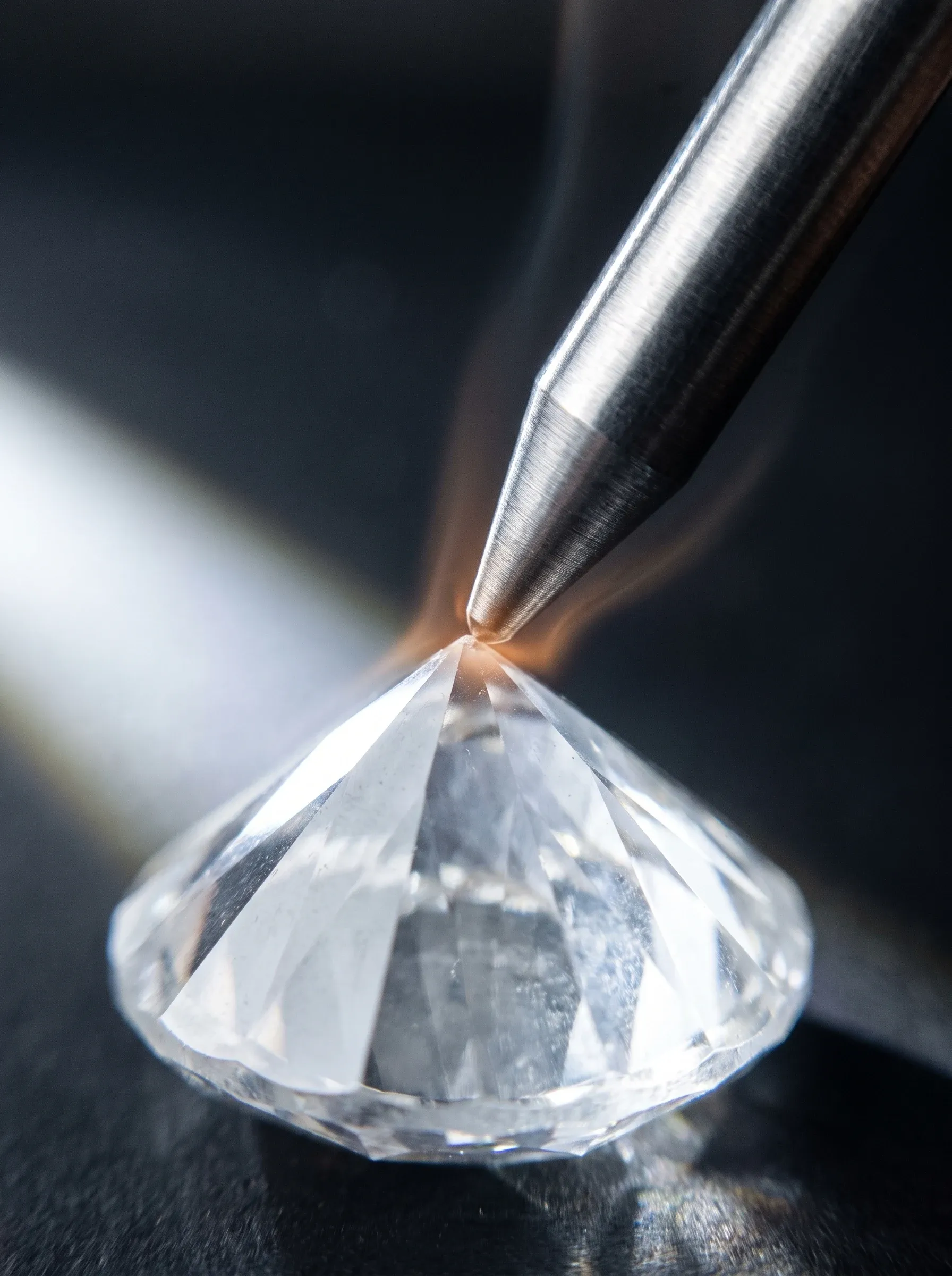 Close-up of a metal tester probe touching the pointed culet of a loose round brilliant stone