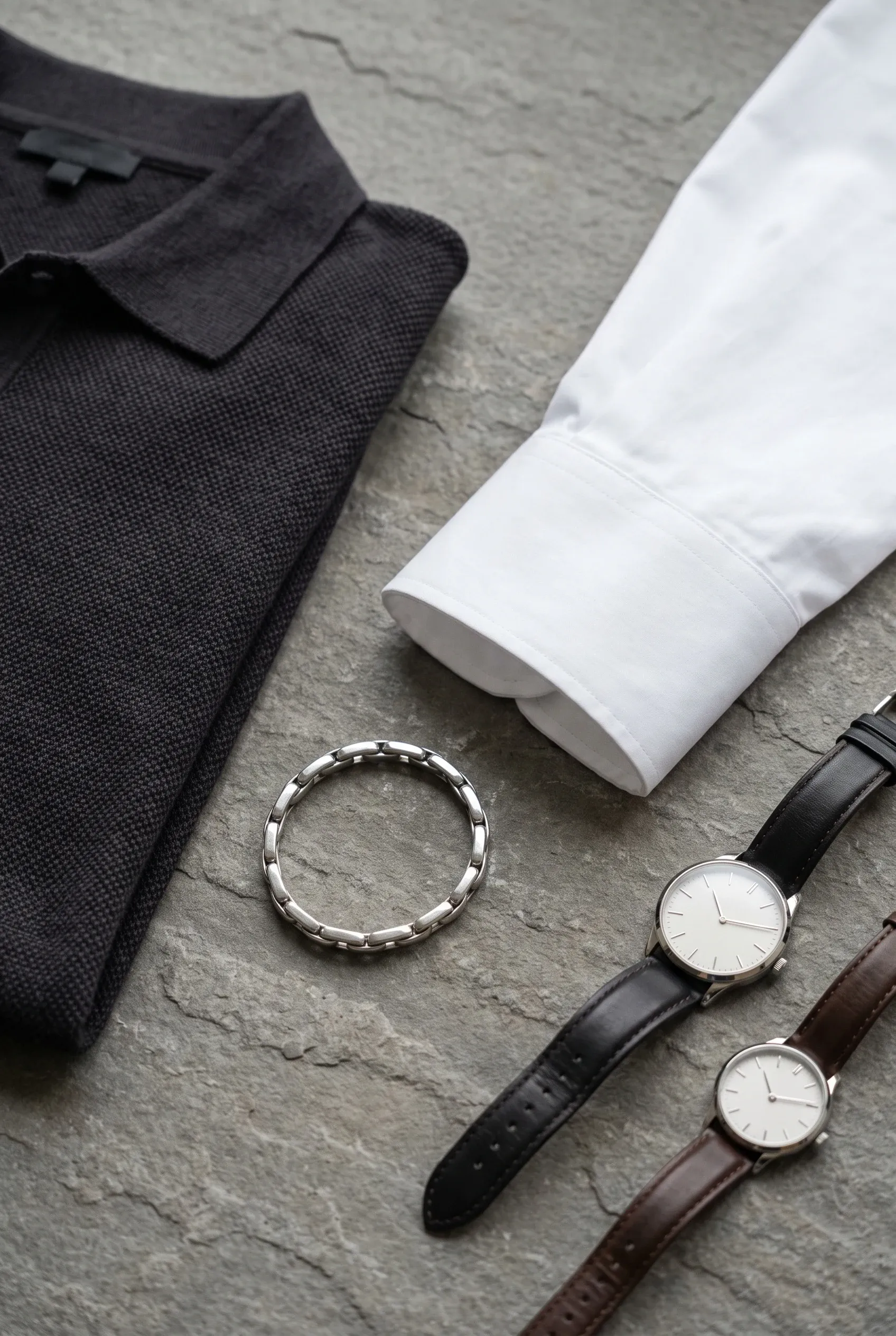 Two differently sized watches styled with a shirt cuff and knit polo in a menswear flat lay.