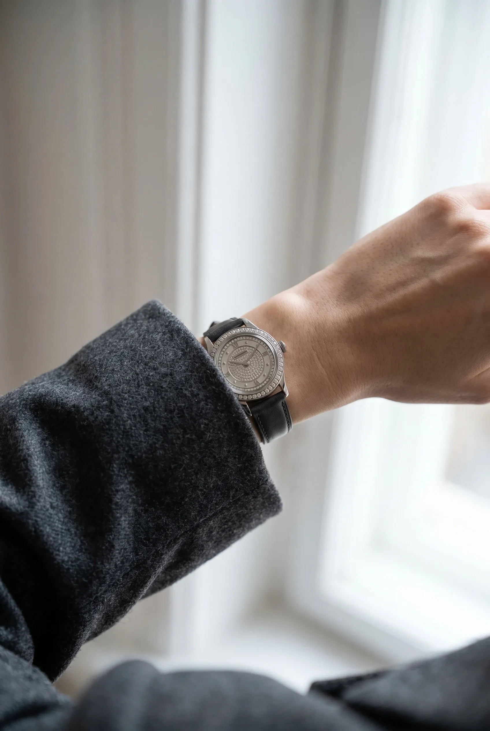 Stone-set watch worn under a cuff on a slim wrist, showing balanced case size and bracelet drape